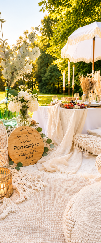 Picknick mit niedrigem Tisch, hellen Sitzkissen, Laternen und weißem Sonnenschirm